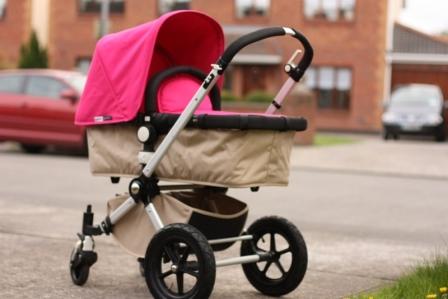 Bugaboo Bee Review: A vibrant pink Bugaboo Bee stroller stands on a sidewalk with residential buildings and a parked car in the background, demonstrating that the Bugaboo Bee has an urban appeal.