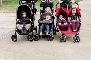  Children riding in a trio of strollers, including a Britax B-Ready, on a concrete path.