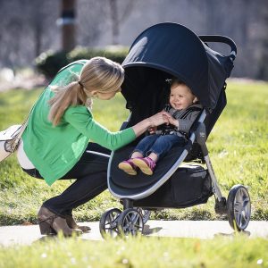 A smiling baby secured in a B-Ready stroller interacts with a crouching adult on a sunny pathway.