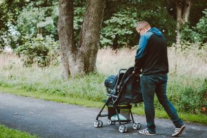 A parent strolls through a park with a Britax B-Ready stroller on a paved path, surrounded by greenery.