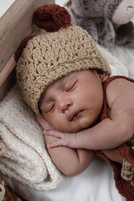 An infant wearing a crocheted beanie while laying comfortably on its side.