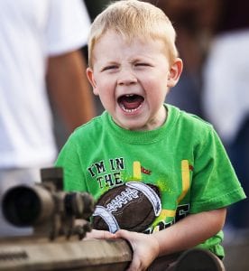 child crying and maybe shouting because he wants something he cannot get, with a green t-shirt that has a football. very expressive face