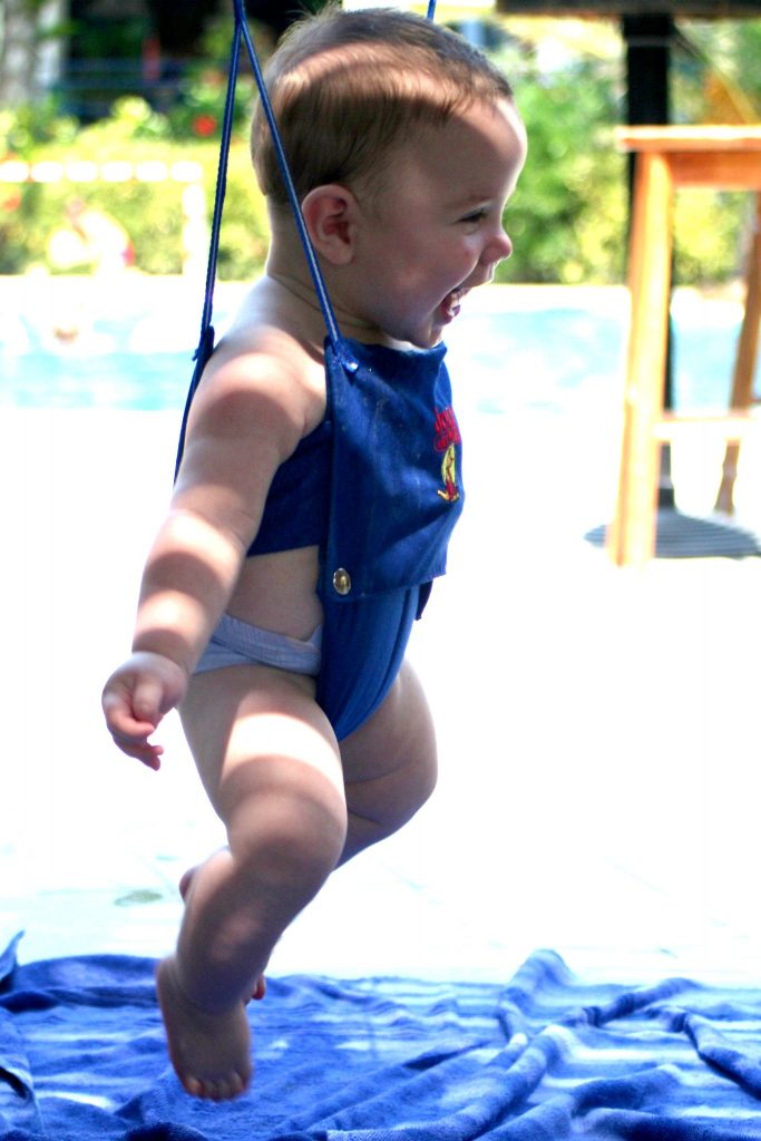 A baby happily jumps while using his baby jumper toys outdoors on a bright day.