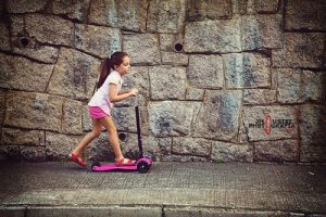 kid riding a pink scooter with a smile on her face
