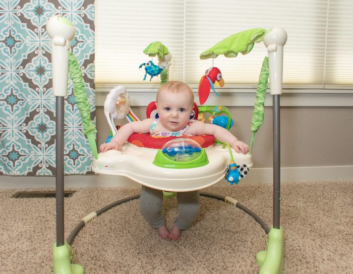 A little child rides on one of the top baby jumpers on the carpeted floor while looking so relaxed in a brightly lit living room. 