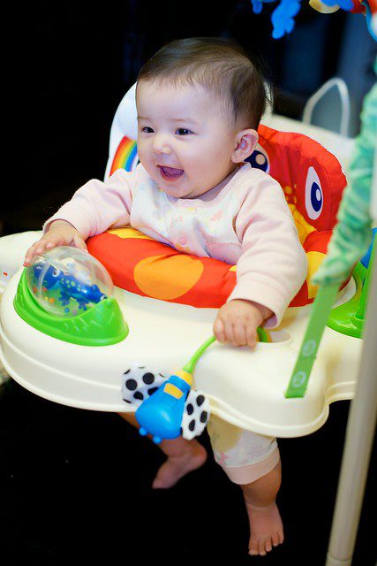 A little boy smiling while riding his colorful baby jumper toy.