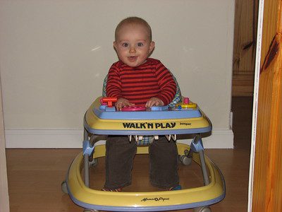 A little boy in striped shirt smiles while riding his toy. 