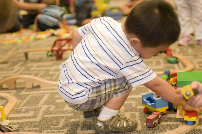 Best toys for 3-year-old boys. The picture captures a little lad engrossed in an engaging activity of gently lifting up a miniature play vehicle.