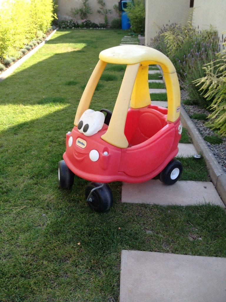 A red and yellow pedal car with a smiley face in front of it in the yard, little tykes toy cars usually patronized by kids all over the world