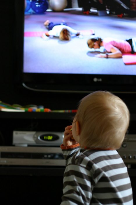 A child looking at the television watching DVDs. The child is wearing stripe sweater. 