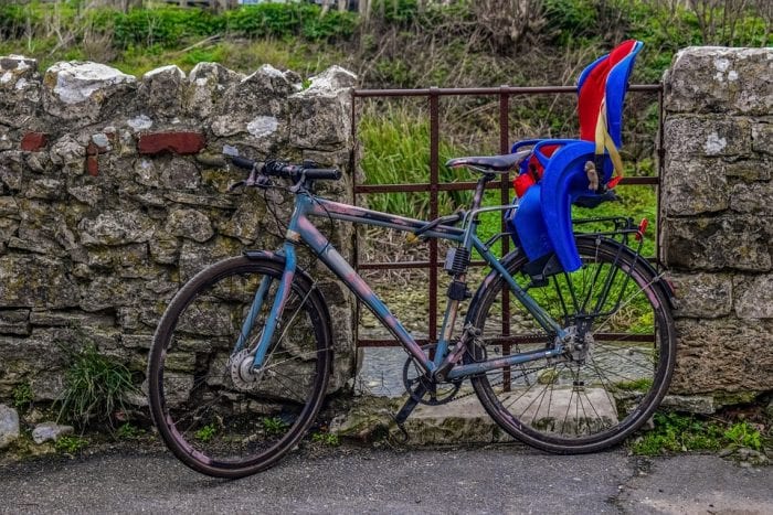 A baby carrier with a blue and red color is attached at the back of the mountain bike.