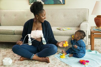 ameda finesse vs medela: A mother pumps milk in the living room. 