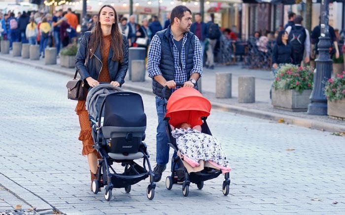 Parents pushing 2 Nuna strollers with babies while travelling. 