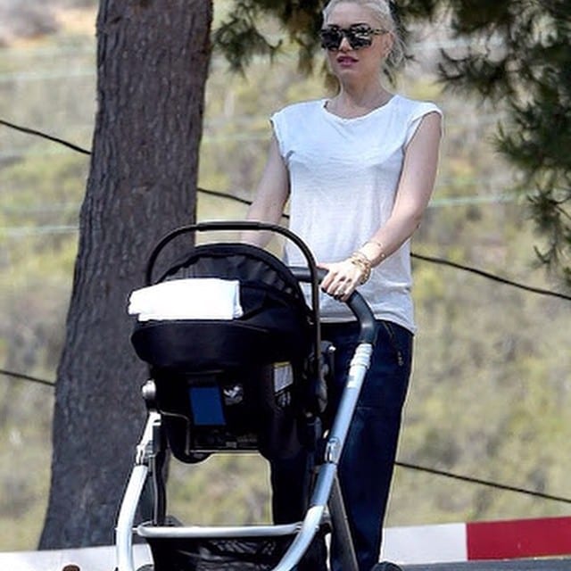 A mom carries her baby in a Nuna carriage while walking outdoors.