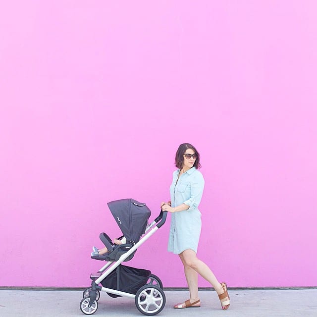 A mom wearing sunglasses pushes a carriage while walking outdoors. 