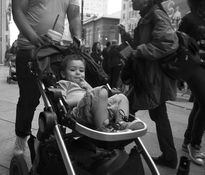 A child in a stroller while being pushed by his father while they go around the city.