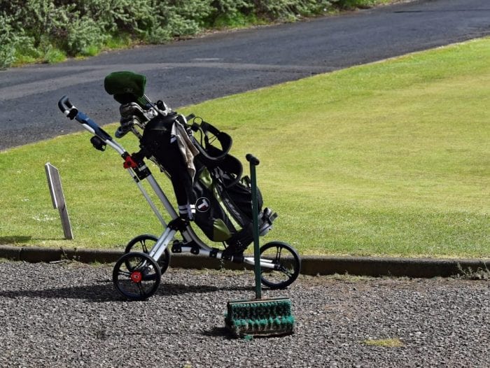 A striking image unfolds of a sleek jogging travel product system placed on a winding asphalt road that meanders through breathtaking greenery. The sports style with small bicycle wheels and adjustable suspensions, glistens under the soft glow of the sun, awaiting its next adventure. Behind it, lush rolling green fields webbed with enchanting trails system.