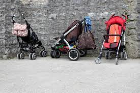 Wheel Stroller: They’re parked in front of a weathered brick wall. The stroller have different colors: the one on the left stroller is black, the stroller in the middle is red, & the stroller on the right is blue.