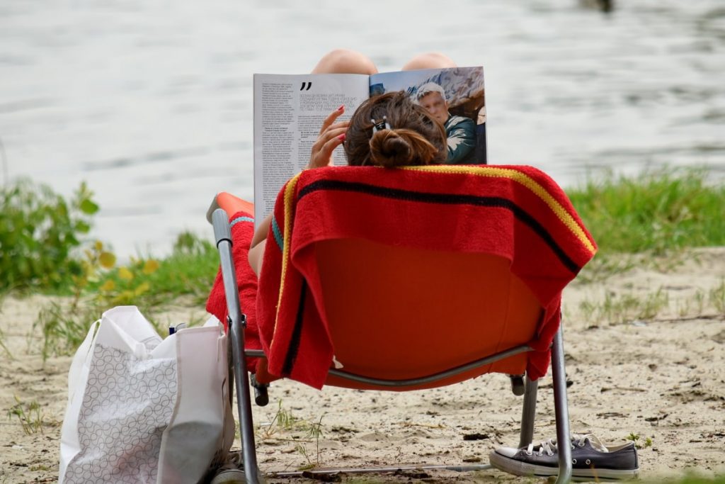A mommy sitting near the seaside with a large luggage on her side.