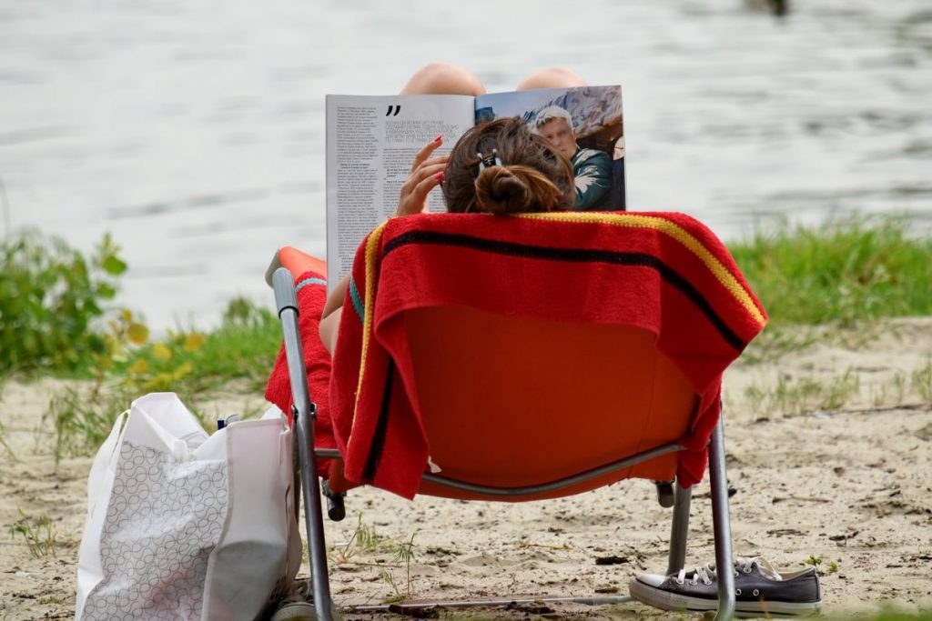 A mom sitting near the beach with a large best beach bag for moms on her side. 