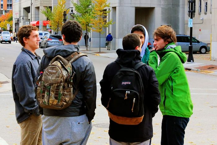 A quintet of young males are convening and during their interaction, they are learning about the best rolling backpack for nursing students!