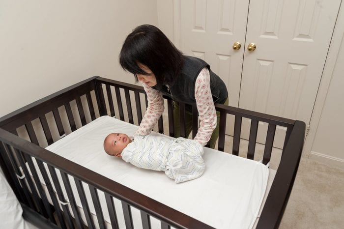 A mom putting her baby carefully in the crib.