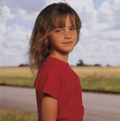 An eleven-year-old girl wearing a red shirt smiles while looking right straight in the camera. 