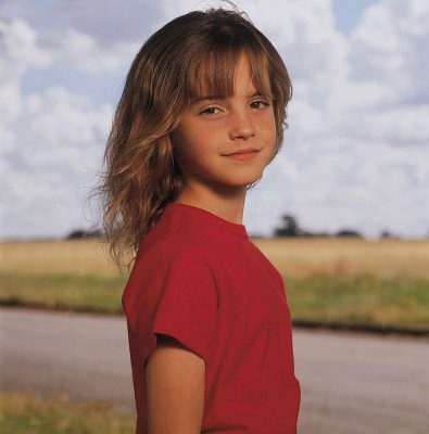 An eleven-year-old girl wearing a red shirt smiles while looking right straight in the camera.