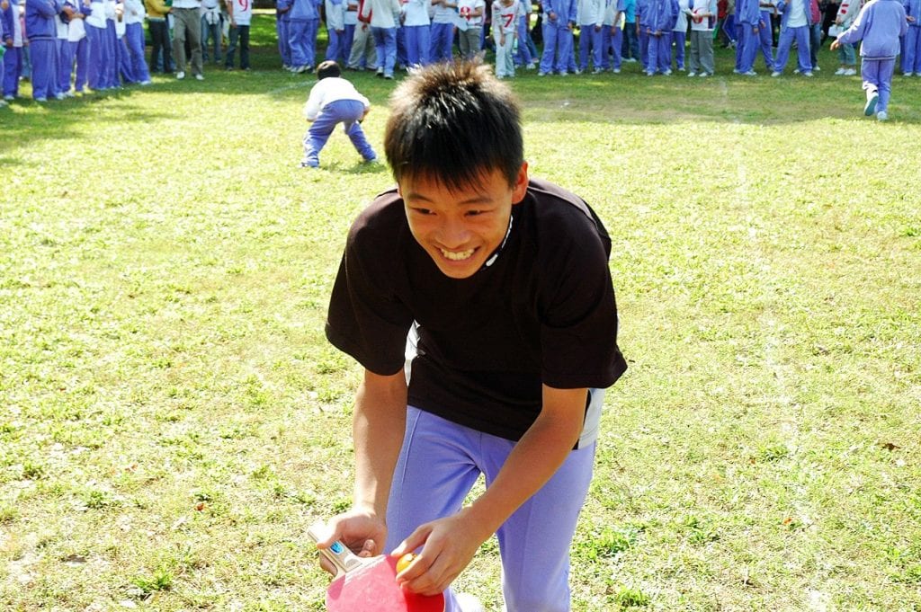 An 11-year-old boy wearing a black shirt smiles while playing outdoors on a bright day. 