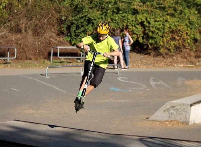 A boy wears a yellow helmet while paying scooter outdoors on a bright day.