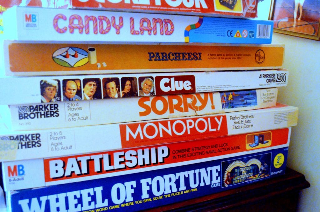 Different kids' board games pile together on the table in a brightly lit room.