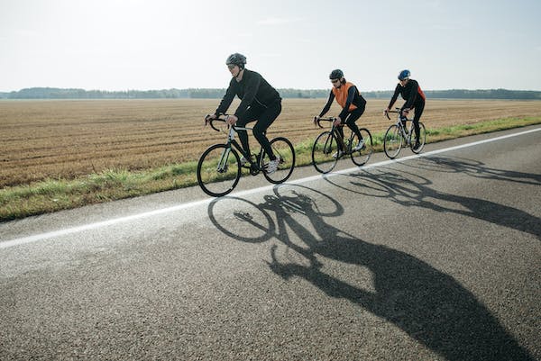 Top three bicyclists riding in a line with a field in the background using their bikes