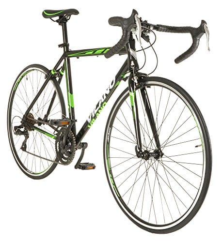 The image shows a black and green Vilano R2 bike. The bike has a black frame with green accents on the wheels, seat post, and handlebars. The bike is leaning against a white wall in a well-lit room. There is a small amount of shadow on the ground from the bike. The image is well-lit and in focus. The colors of the road bike are accurate and the bike is clearly in focus. The background is white, which makes the bike stand out.