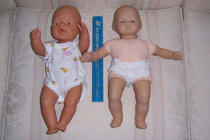 There are two infant dolls. The one looks like he's asleep and the other is not. They are wearing different clothes.