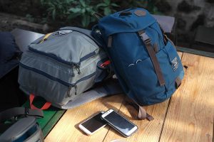 Backpack: Two backpacks on a wooden table, one gray and one blue, with a smartphone lying beside them, suitable for nursing students.