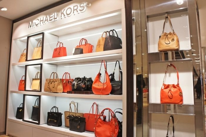 Display of various Michael Kors designer bags on shelves in a retail store.