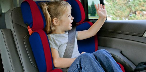 A kid in ponytail waves her hand while riding the car happily. 