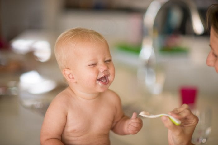 The baby smiles while his mother is feeding him with best yogurt suitable for babies. 