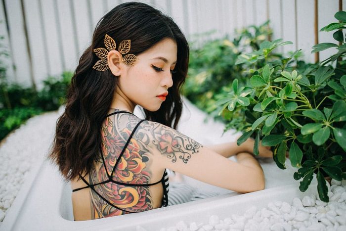 A woman in a bathtub with colored back tattoos.