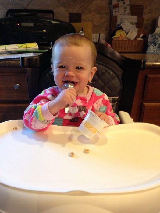 A happy child eating yogurt on her table.