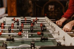 A person's hand playing with red team figures on a foosball table, engaging in the best football table game.