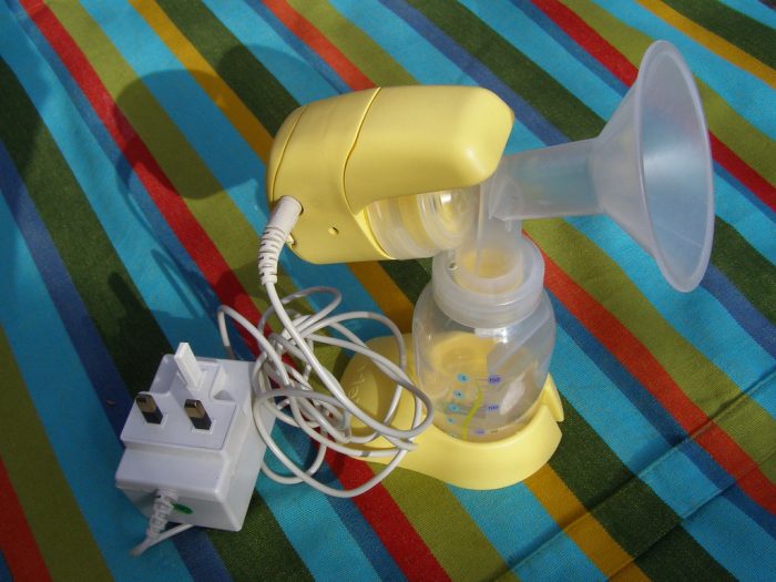 A yellow breast pump placed by a mom on a colorful striped bed ready to be used for pumping breastmilk. 