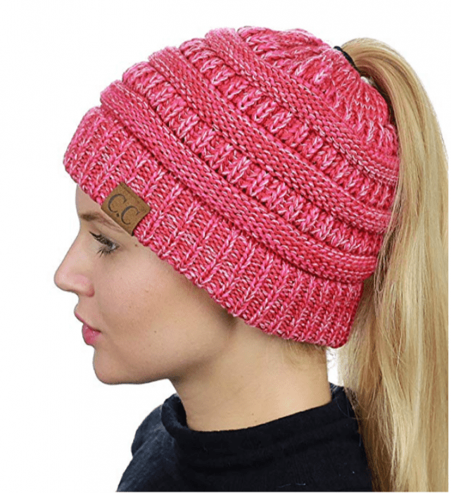 A girl with blond hair wears a pink ponytail beanie and looks into the distance