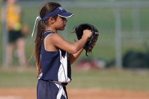 A girl playing baseball while wearing a baseball glove.