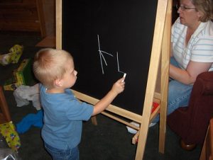 A toddler in a blue shirt uses the best easel for kids while practicing writing letters. This easel makes the toddler's writing easier. 