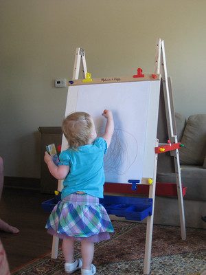 A toddler uses her best easel. This best easel makes toddler's writing easier.