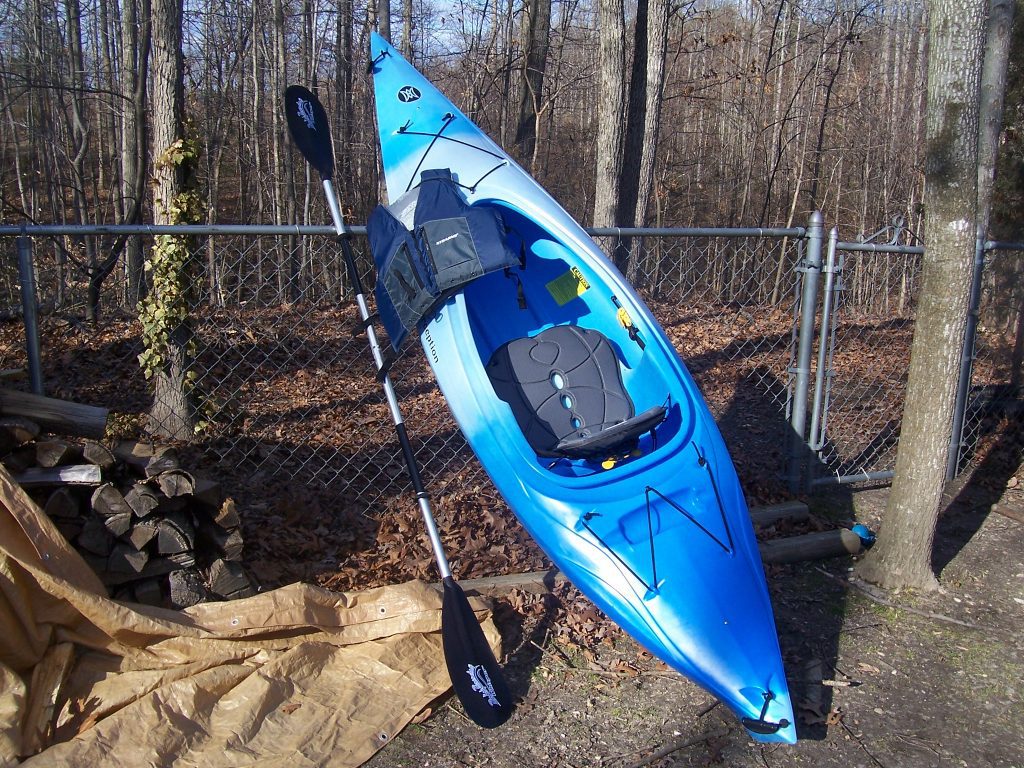 A kayak and a paddle leaning against a fence.