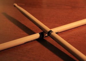 A pair of crossed sticks on a wooden surface, under a warm light, representing some of the best drumsticks for beginners.