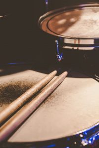 A pair of sticks, considered among the best drumsticks for beginners, resting on a snare drum with other drum set elements softly blurred in the background.