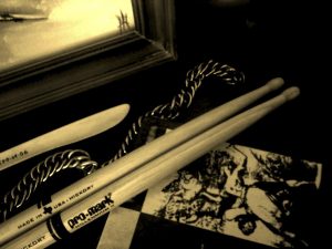 A sepia-toned image featuring drum sticks and a twisted drum brush, possibly among the best drumsticks for beginners, resting on a surface with printed images, evoking a nostalgic musical atmosphere. Truly the best drumsticks for beginners.